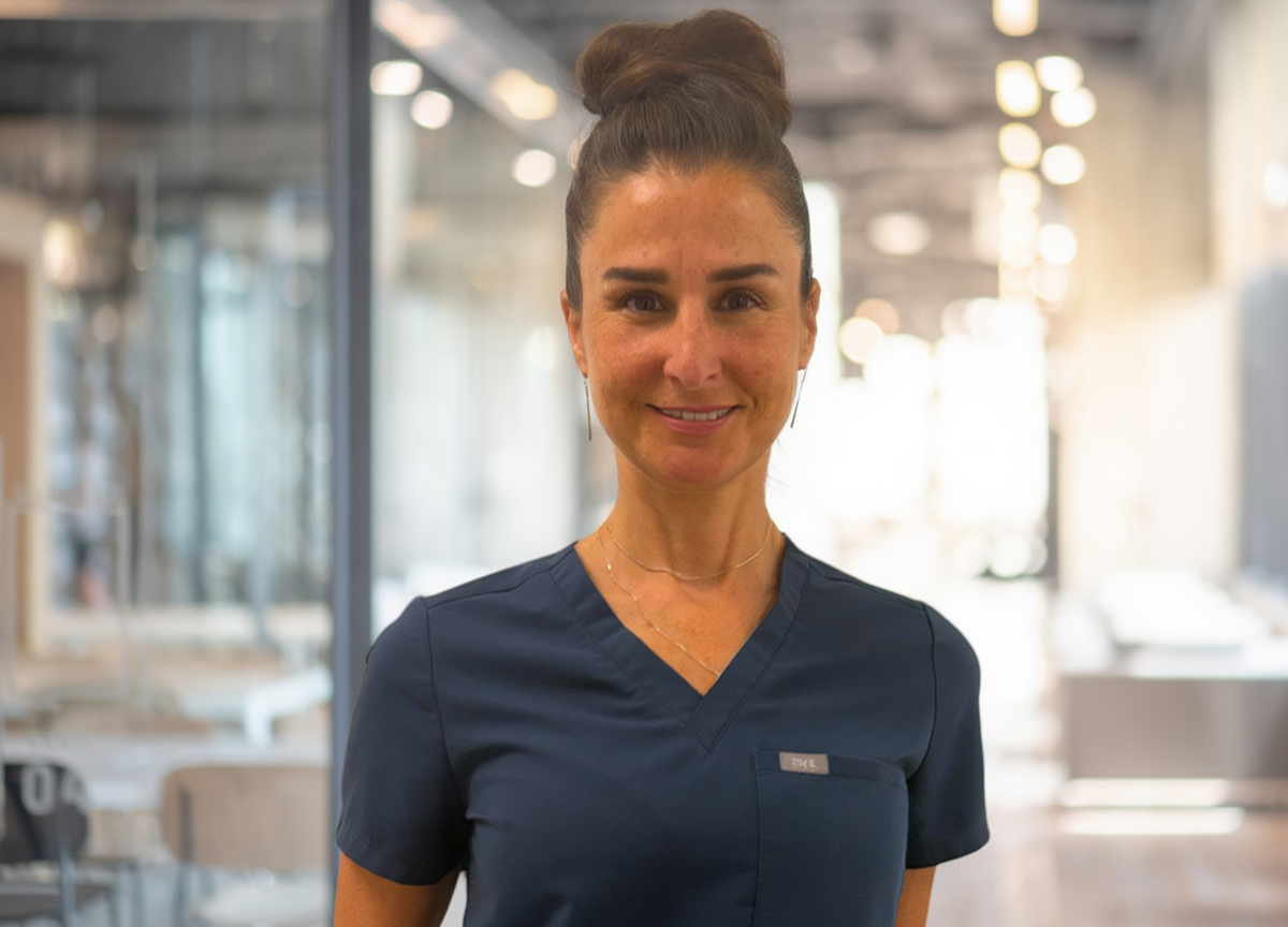 Healthcare professional in navy scrubs smiling in a bright clinic hallway.