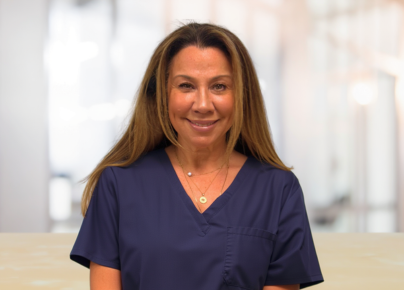 Smiling female healthcare worker in navy scrubs in a bright clinic setting.