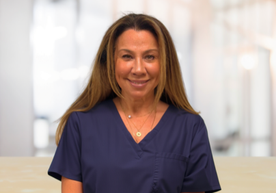 Smiling female healthcare worker in navy scrubs in a bright clinic setting.
